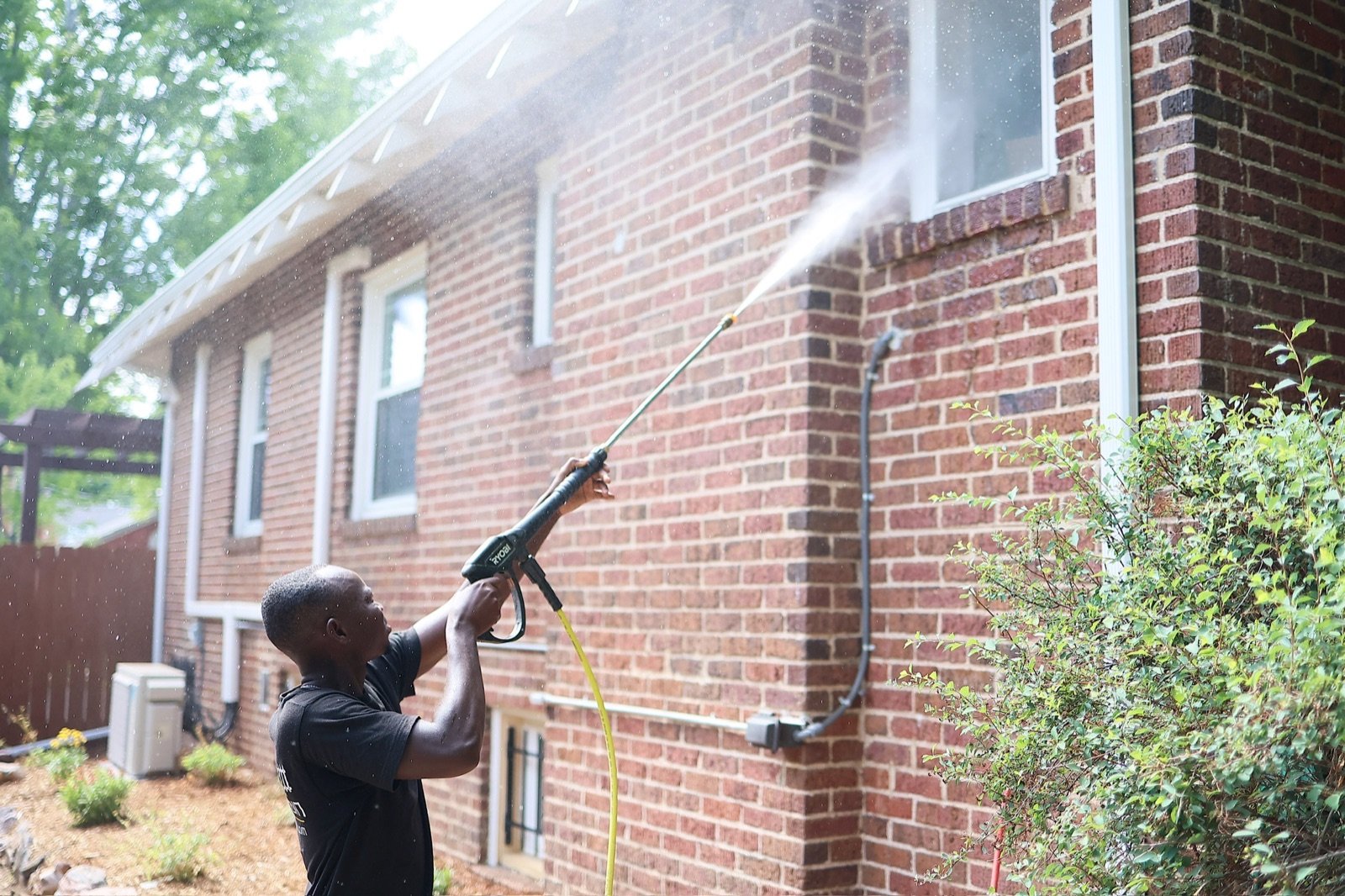 Golden Stain crew member soft washing a brick house exterior