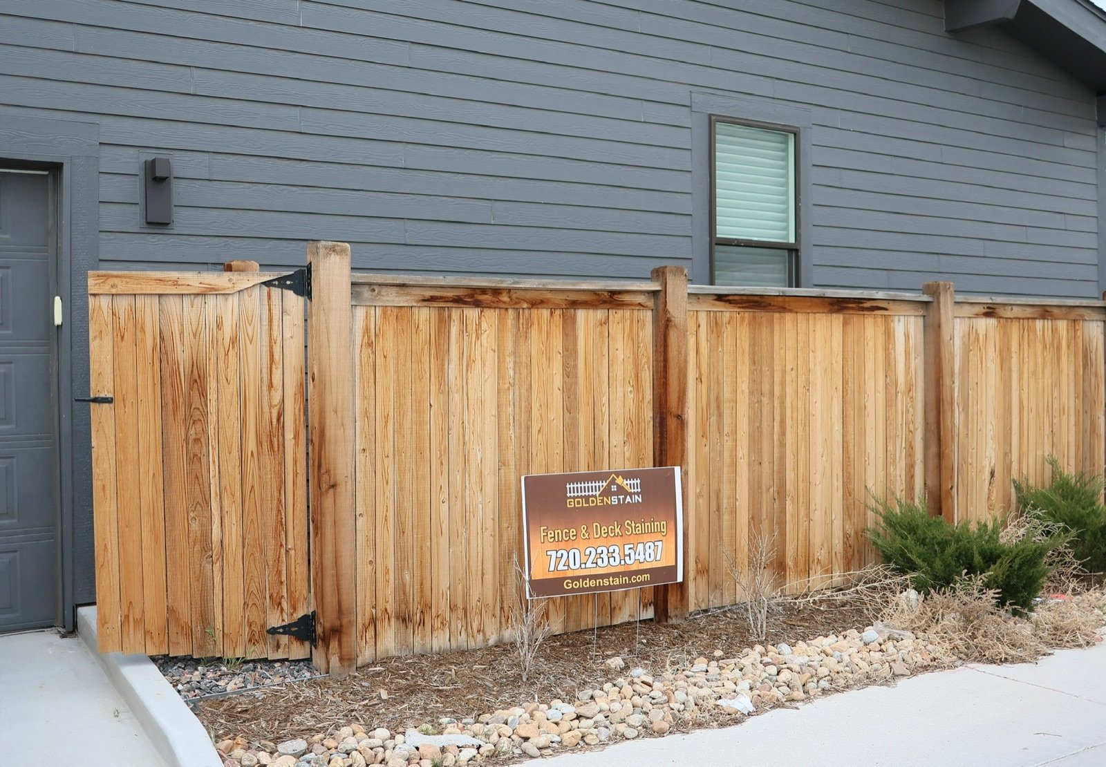 Neat stained cedar fence along a sidewalk with a Golden Stain yard sign