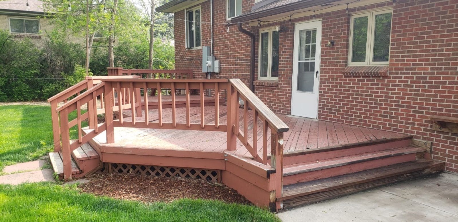 Deck stained in a warm redwood tone beside a brick home